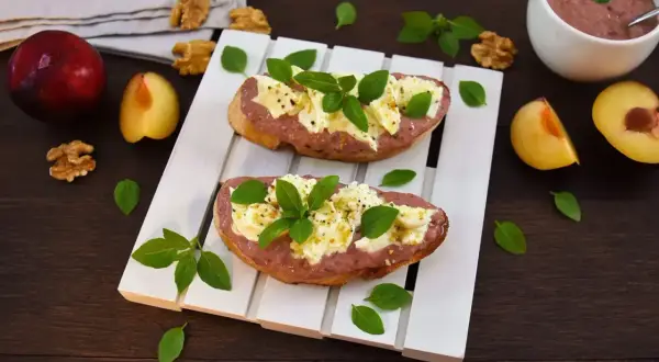Zwei Bruschettas mit Pflaumenaufstrich, Käse und Basilikum, garniert mit Walnüssen und frischen Pflaumen.