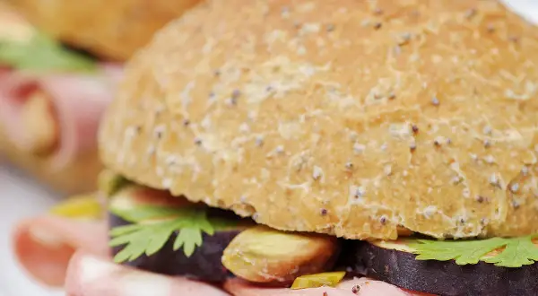Un délicieux sandwich mortadelle garni de tranches d'aubergine, de pistaches et de persil frais, prêt à être dégusté.
