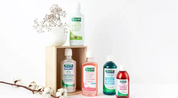 Zestaw płynów do płukania jamy ustnej GUM, w tym ActiVital, Original White, SensiVital+ i Paroex, obok delikatnych kwiatów.