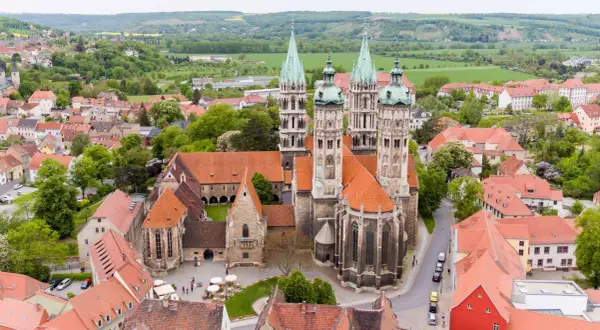Der Naumburger Dom, ein Meisterwerk romanischer Architektur, thront über der Stadt. Seine Türme ragen in den Himmel, umgeben von roten Dächern und grünen Hügeln.