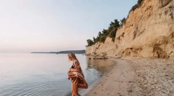 Mujer rubia camina por la playa, sintiendo la brisa marina. Ella anhela la libertad y el deseo de querer viajar sola.