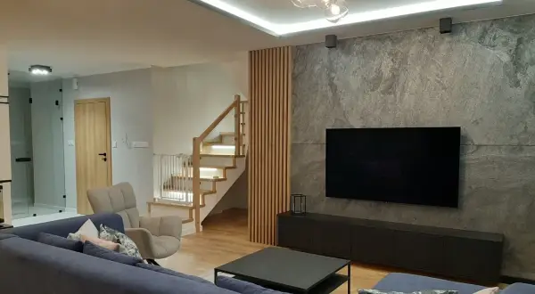 Nowoczesne lamele ścienne aranżacje tworzą ciepłą atmosferę obok kamiennej ściany z TV.