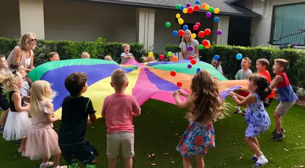 Children joyfully engage in gross motor activities for toddlers, tossing colorful balloons into the air while holding a large parachute.