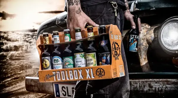 Mężczyzna z tatuażami niesie skrzynkę "TOOLBOX XL" z różnymi butelkami piwa. Idealne połączenie: jakie butelki do jakich skrzynek.
