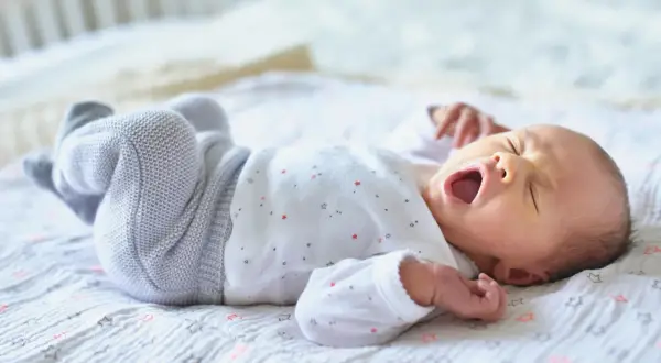 Ein Baby gähnt auf einer Decke mit Sternen. Wann Babys alleine einschlafen, ist eine Frage, die viele Eltern beschäftigt.