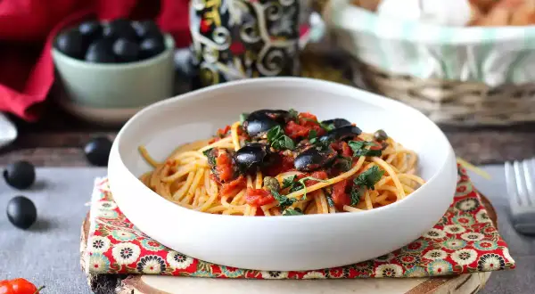En skål med spaghetti puttanesca, toppad med svarta oliver och persilja. Ett härligt recept för en smakrik middag.