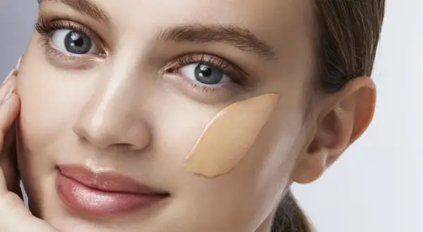 Una donna con un tocco di fondotinta sulla guancia, un esempio visivo di come applicare il fondotinta per un look naturale.
