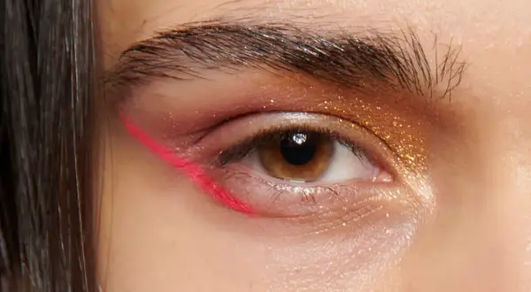 Occhio con eyeliner fucsia audace e ombretto dorato scintillante. Un look di trucchi per gli occhi che cattura l'attenzione.