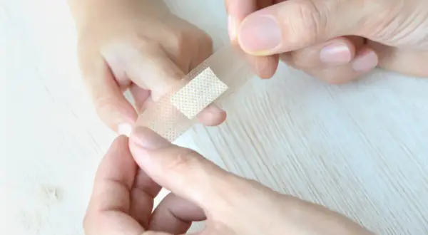 Ręce przyklejają plaster na palec dziecka, by pomóc mu jak oduczyć dziecko ssania palca przy zasypianiu.