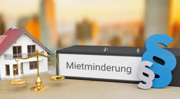 Hausmodell, Waage und Aktenordner mit "Mietminderung" beschriftet. Ein Paragraphenzeichen symbolisiert das Recht bei Mietminderung von Kalt- oder Warmmiete.