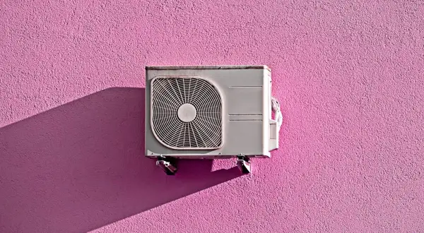 Unità esterna di condizionatore appesa a un muro rosa acceso, con ombra proiettata. Pensando allo smaltimento condizionatori.