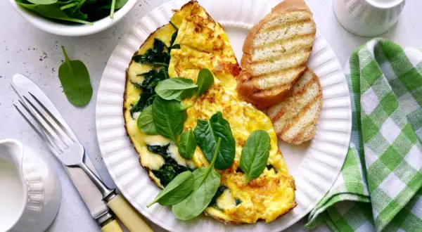 Pyszny omlet ze szpinakiem, podany z grzankami i świeżymi liśćmi szpinaku. Idealny na zdrowe śniadanie.
