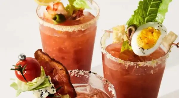 Tre glas med Bloody Mary, dekorerade med räkor, ägg, bacon och grönsaker. En festlig brunchdrink!