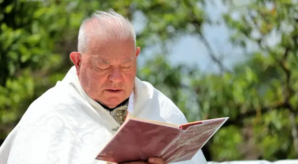 Kapłan w białej szacie zamyślony nad księgą, w jego oczach widać żal za grzechy.
