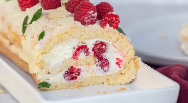 Saftige Biskuitrolle mit frischen Himbeeren und Sahne gefüllt, garniert mit Beeren und Mandelblättchen. Ein Genuss!