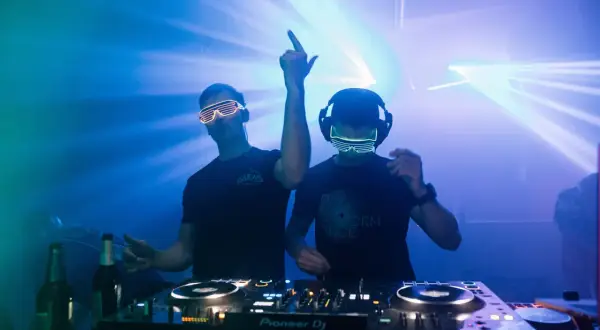 Dwóch DJ-ów w neonowych okularach gra muzykę trance na imprezie z laserami.