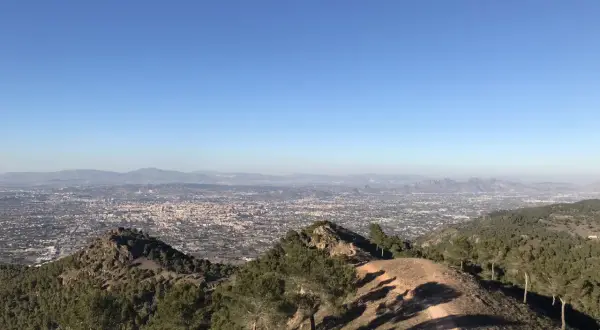 Vista panorámica desde la sierra de carrascoy, con un extenso paisaje urbano y montañas al fondo bajo un cielo azul despejado.