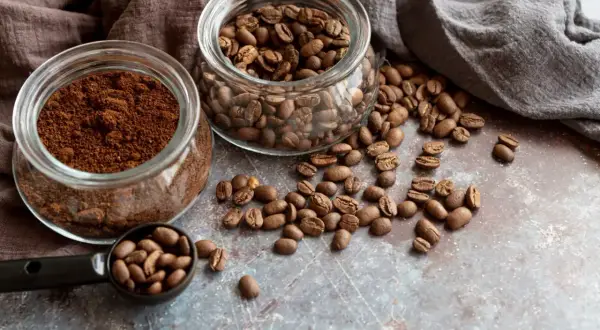 Due barattoli di vetro, uno con caffè macinato e l'altro con caffè in grani, con chicchi sparsi. Quale scegliere per il tuo caffè perfetto?