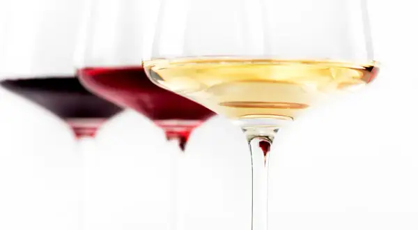 Trzy kieliszki z winem: ciemnoczerwonym, rubinowym i białym. Wino się pieni, tworząc subtelne refleksy.