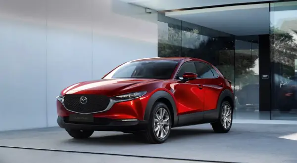 Elegancka, czerwona Mazda CX-30 błyszczy przed nowoczesnym budynkiem z dużymi oknami.