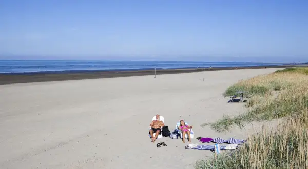 Två personer solar på stranden vid Björkäng camping. En man och en flicka njuter av solen.