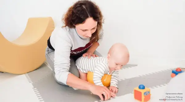Mama wspiera roczne dziecko w nauce raczkowania. Radosne zabawy z maluszkiem na macie.