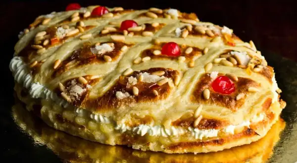 Deliciosa coca de San Juan rellena de crema, decorada con piñones, cerezas rojas y azúcar.
