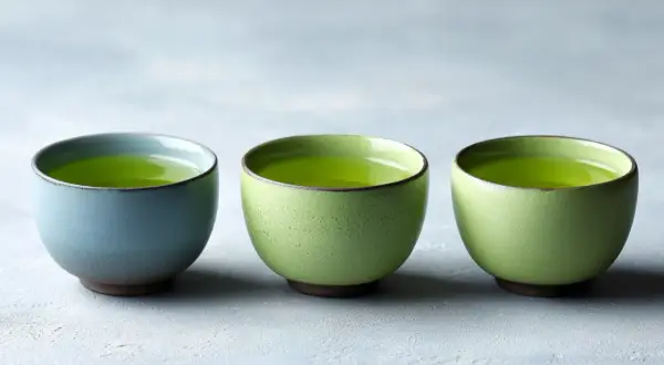 Trois tasses de thé vert vif, une bleue et deux vertes, suggérant la dose maximale de thé vert par jour pour une dégustation paisible.
