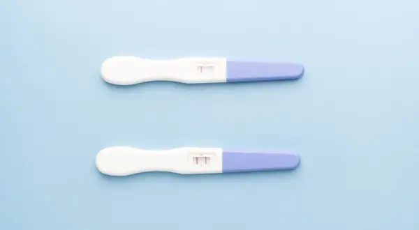 Dwa testy ciążowe na jasnoniebieskim tle. Jeden pokazuje jeden pasek, drugi dwa. Kiedy zrobić test ciążowy?