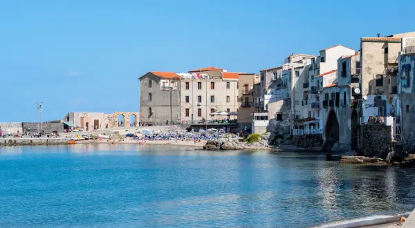 Edificios antiguos y una animada cefalu playa con gente disfrutando del sol y el mar azul.