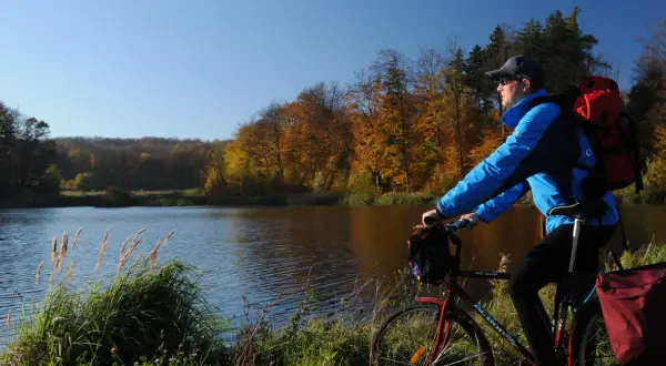 Jesień sprzyja jednodniowym wycieczkom rowerowym. Rowerzysta z plecakiem podziwia jesienne barwy lasu nad jeziorem.