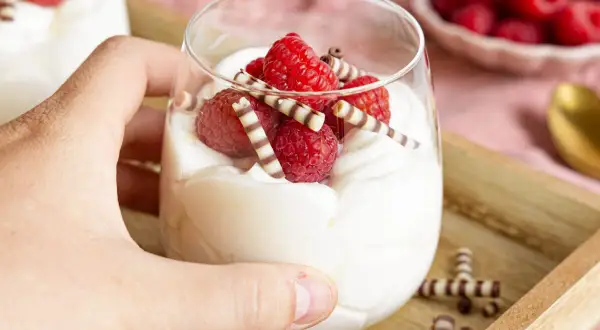 Ein Glas mit cremigem Quark-Dessert, garniert mit frischen Himbeeren und Schokoröllchen.