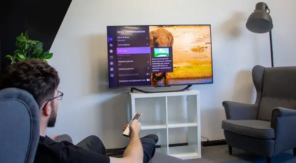 Mężczyzna siedzi w fotelu i ogląda telewizor z menu ustawień obrazu.