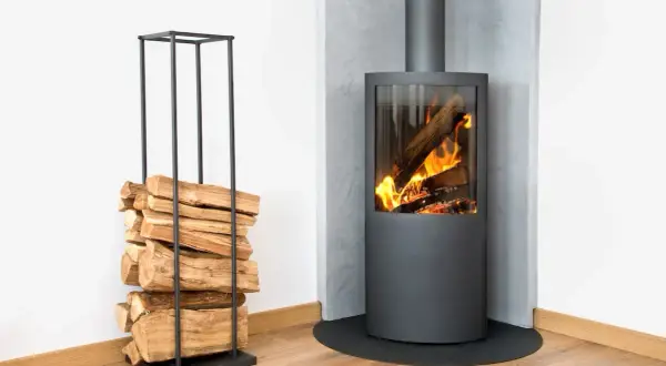 Poêle à bois moderne avec une cheminée d'évacuation par le mur, entouré de bois de chauffage empilé dans un support élégant.
