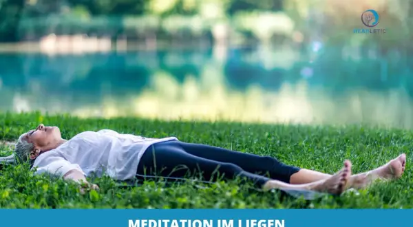 Frau genießt eine friedliche Meditation im Liegen auf einer grünen Wiese am See.