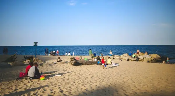 Ludzie odpoczywają na plaży nad morzem. Choć Szczecin nie leży bezpośrednio nad morzem, jego bliskość jest odczuwalna.