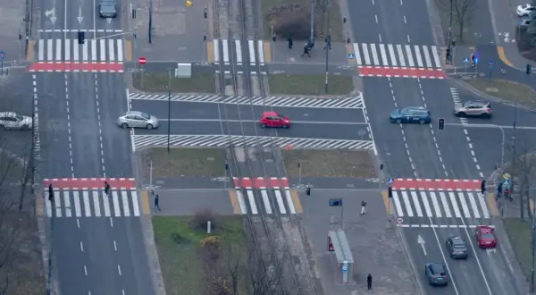 Skrzyżowanie z przejściami dla pieszych. Czerwony samochód jedzie po pasach, zastanawiając się, ile za wyprzedzanie na pasach.