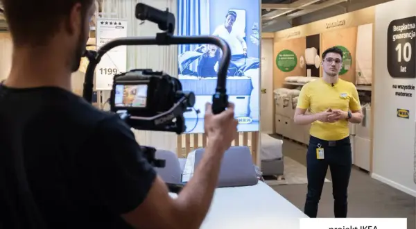 Operator kamery nagrywa pracownika IKEA w sklepie, na ekranie w tle reklama materaca.