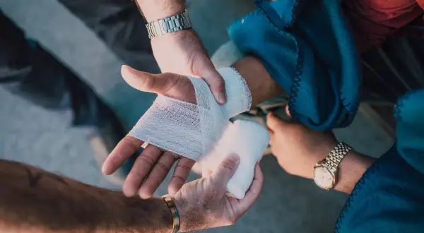 Mains bandant une blessure, peut-être suite à une violence involontaire. L'une des mains est bandée, l'autre tient la compresse.