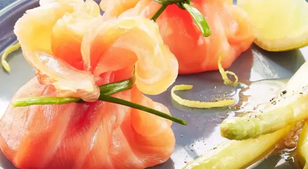 Une délicieuse entrée froide : des fagots d'asperges et de saumon fumé, ornés d'une touche de citron et de ciboule.