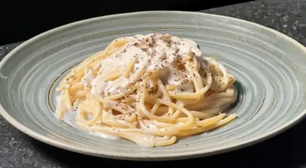 Un plat de tonnarelli cacio e pepe crémeux, saupoudré de poivre noir fraîchement moulu, servi dans une assiette texturée.