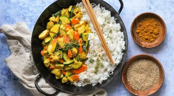 Ein leckeres Curry Geschnetzeltes Rezept mit Reis, Zucchini und Karotten, garniert mit Sesam und Kräutern.