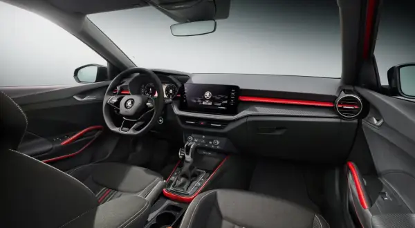 Interni sportivi della Skoda Fabia Montecarlo con sedili in tessuto, volante multifunzione e display centrale. Dettagli rossi accentuano l'abitacolo.