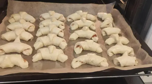 Gotowe do pieczenia rogaliki z marmoladą, ułożone na blasze wyłożonej papierem.