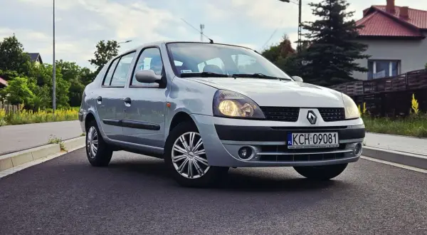 Srebrny Renault Thalia 1.4 z polskimi tablicami rejestracyjnymi KCH 09081 zaparkowany na poboczu drogi.