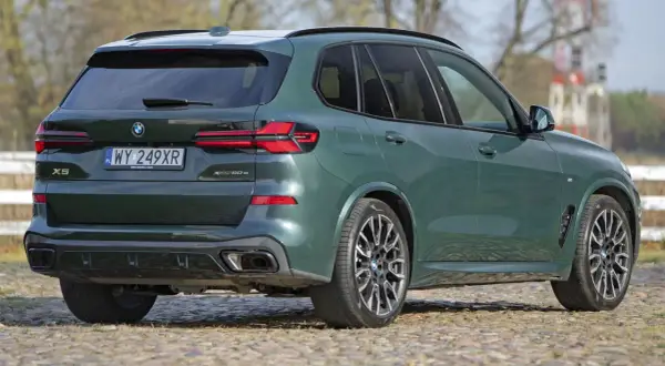 Zielony x5 BMW z napisem XDrive 50e na klapie bagażnika, zaparkowany na bruku.