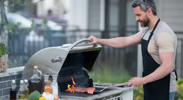 Mężczyzna w fartuchu grilluje łososia na grillu gazowym, pokazując, jak działa grill gazowy.