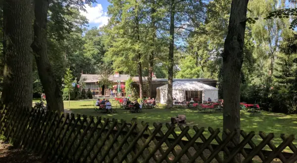 Ein Biergarten im Grünen, mit Gästen an Tischen unter Bäumen und einem Festzelt. Hier findet man **hanffs ruh**.