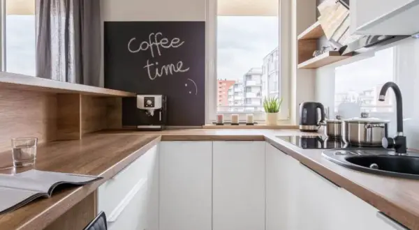 Biała kuchnia z drewnianym blatem, na którym stoi ekspres do kawy. Na tablicy napis "coffee time".