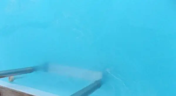 Un rouleau nettoie l'eau trouble d'un bassin bleu vif, laissant des traces blanches.